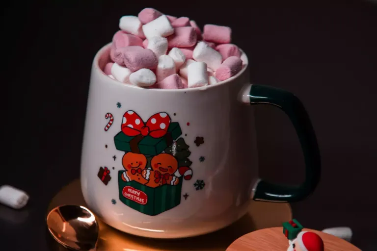 Taza decorada con una caja de regalos y galletas de navidad, en cuyo interior se ven nubes de gominola