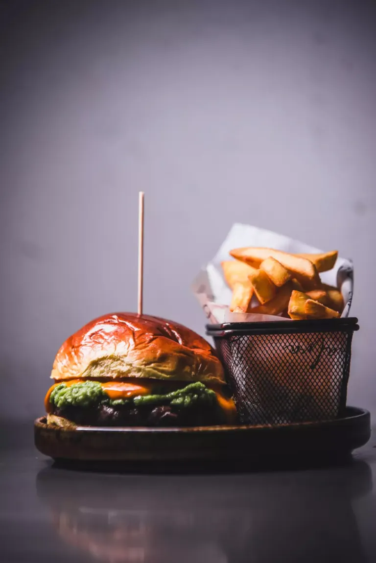 Hamburguesa con carne, aguacate y queso junto a una cesta son con patatas fritas