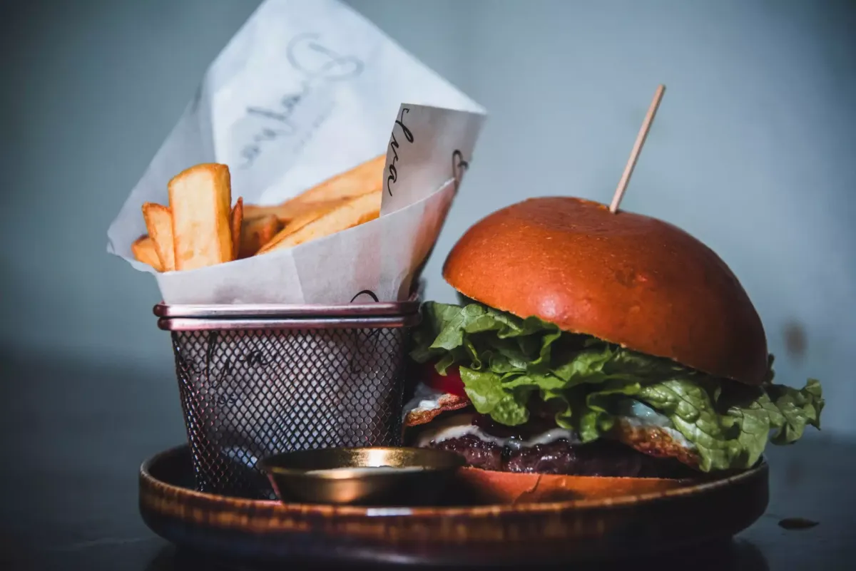 Hamburguesa con carne, bacon, lechuga y queso junto a una cesta son con patatas fritas