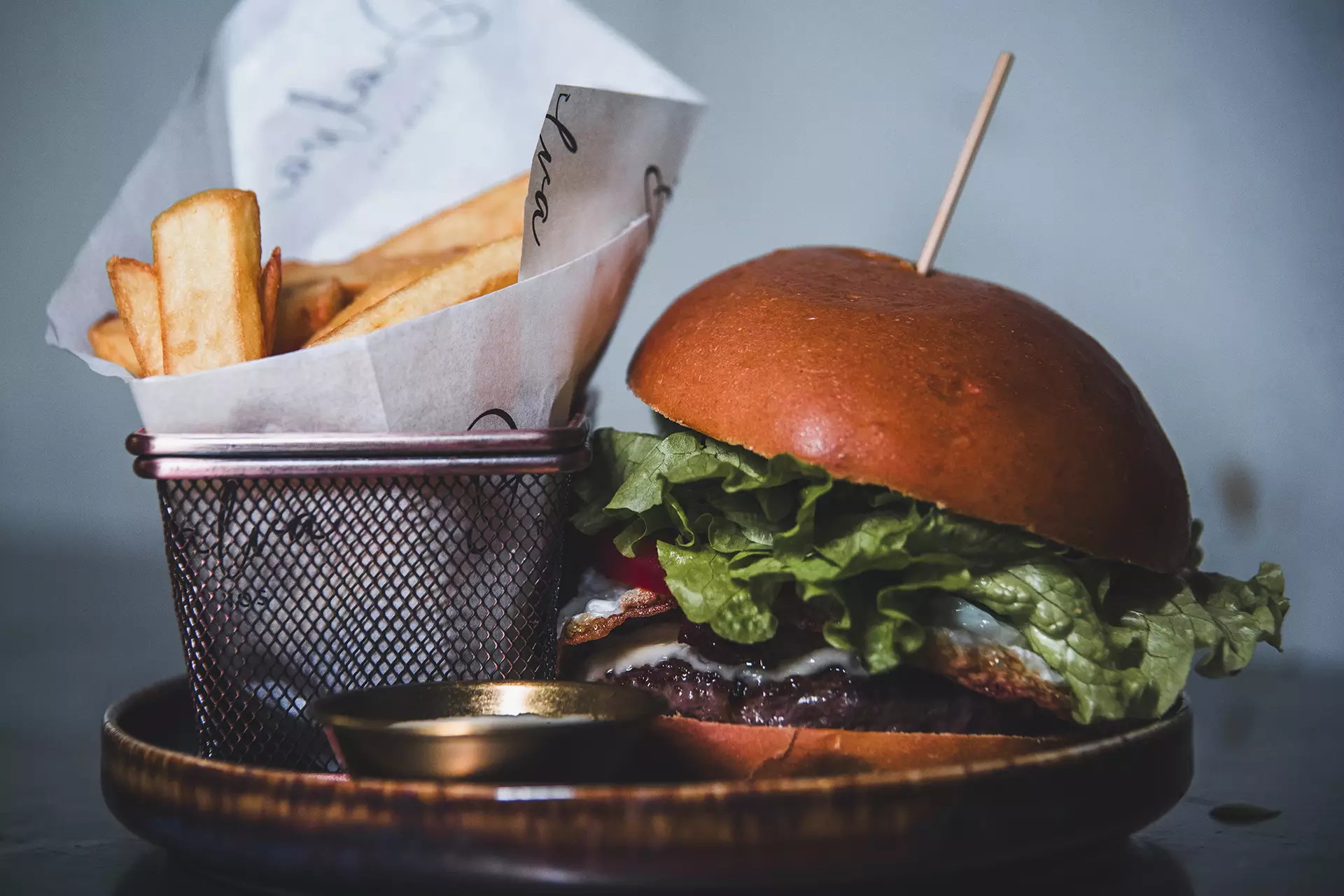 Hamburguesa con carne, bacon, lechuga y queso junto a una cesta son con patatas fritas